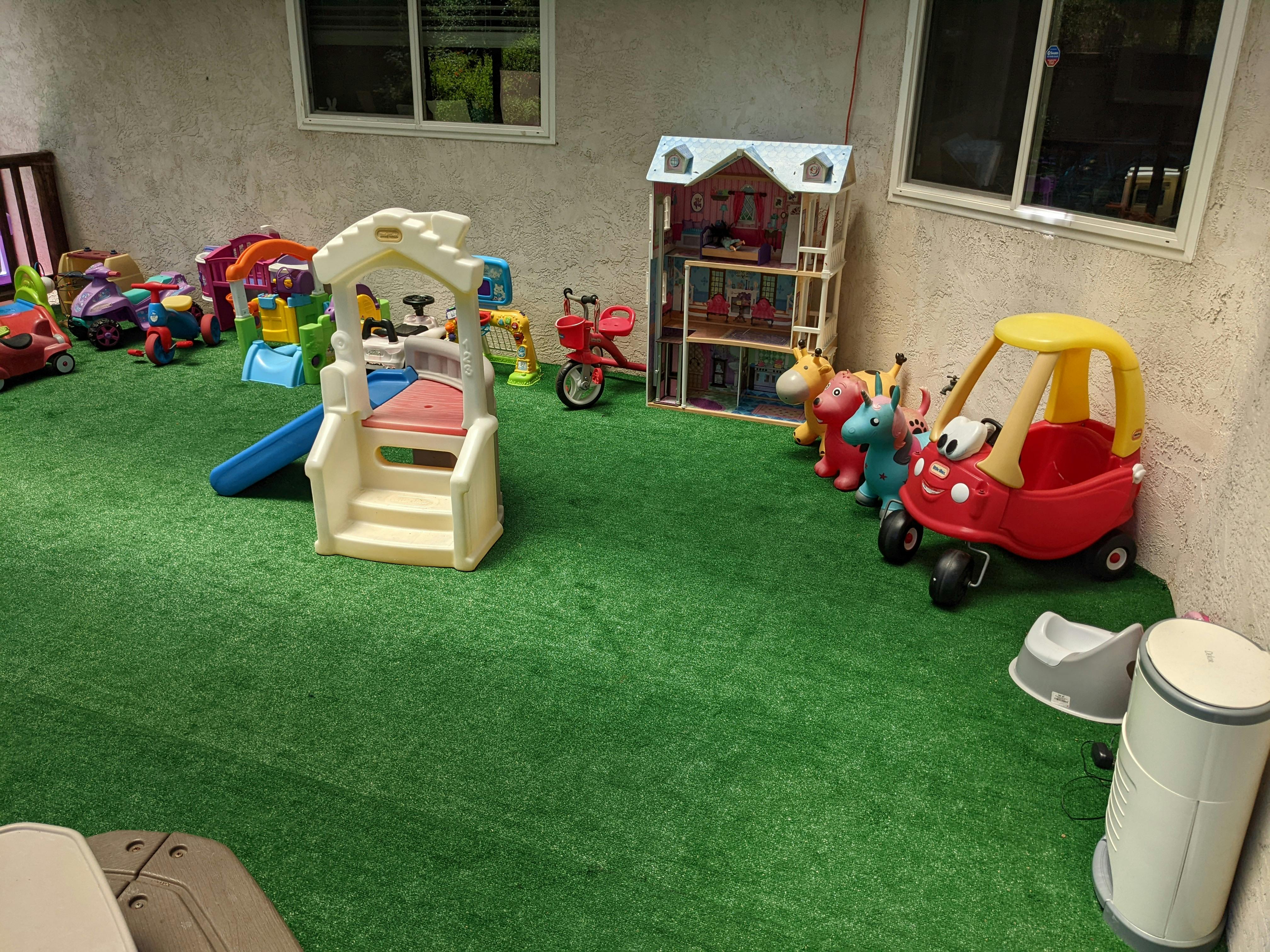 Indoor play area with various toys including a slide, dollhouse, and ride-on car