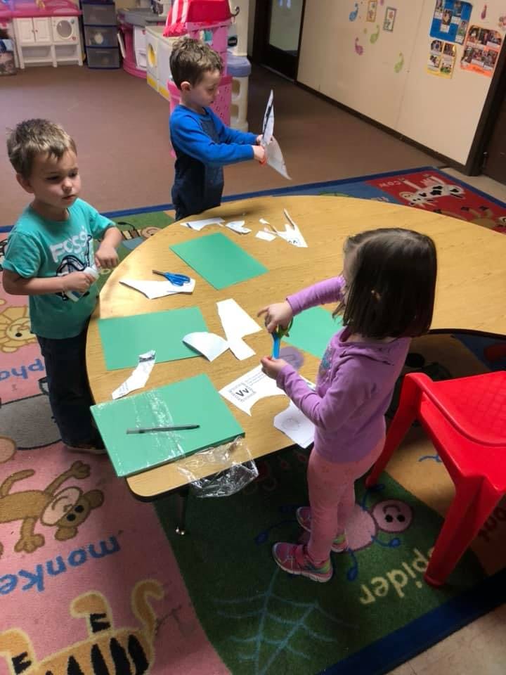 Three children doing crafts at a table in a classroom