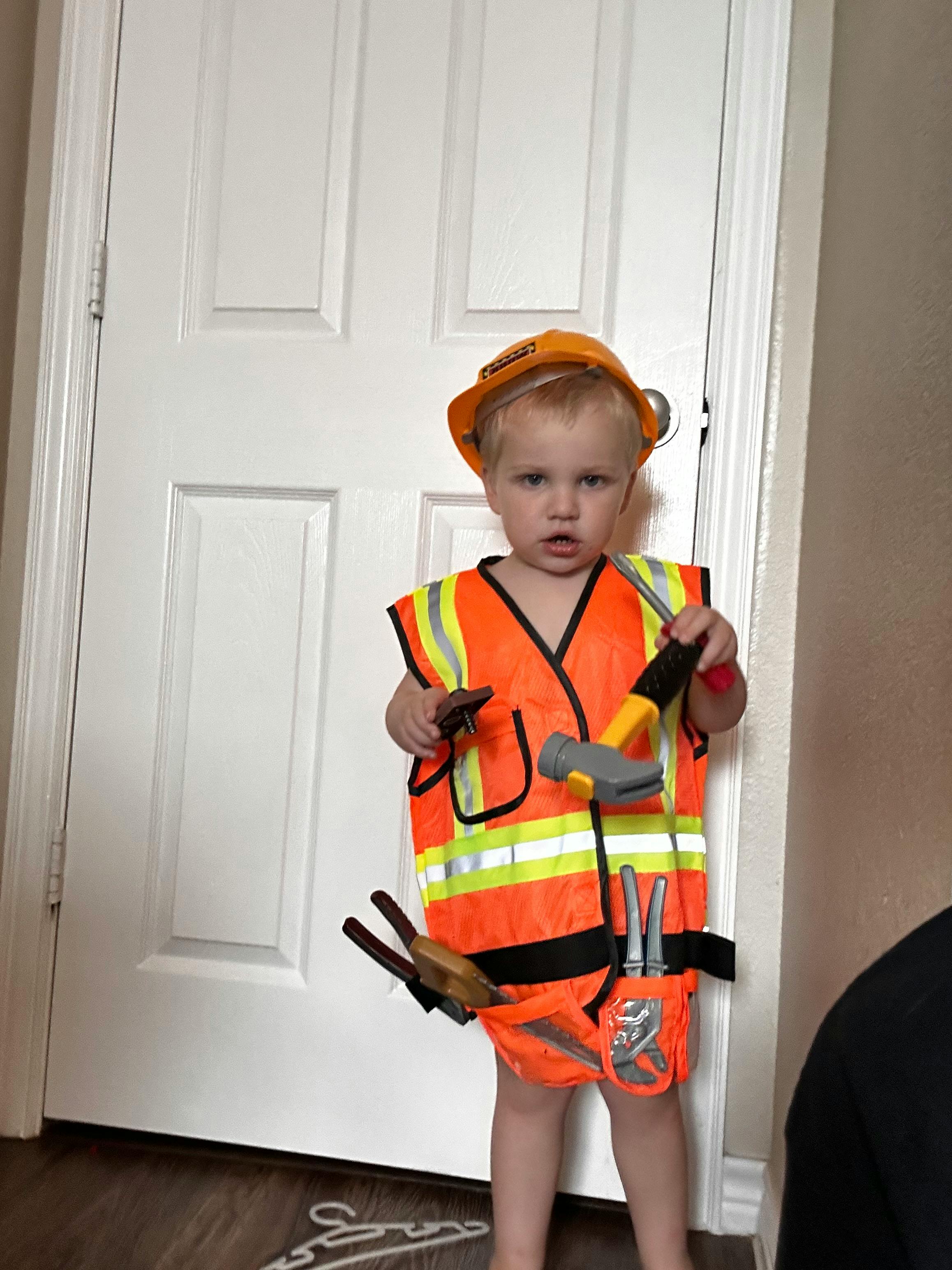 Child in a construction vest and hard hat holding toy tools