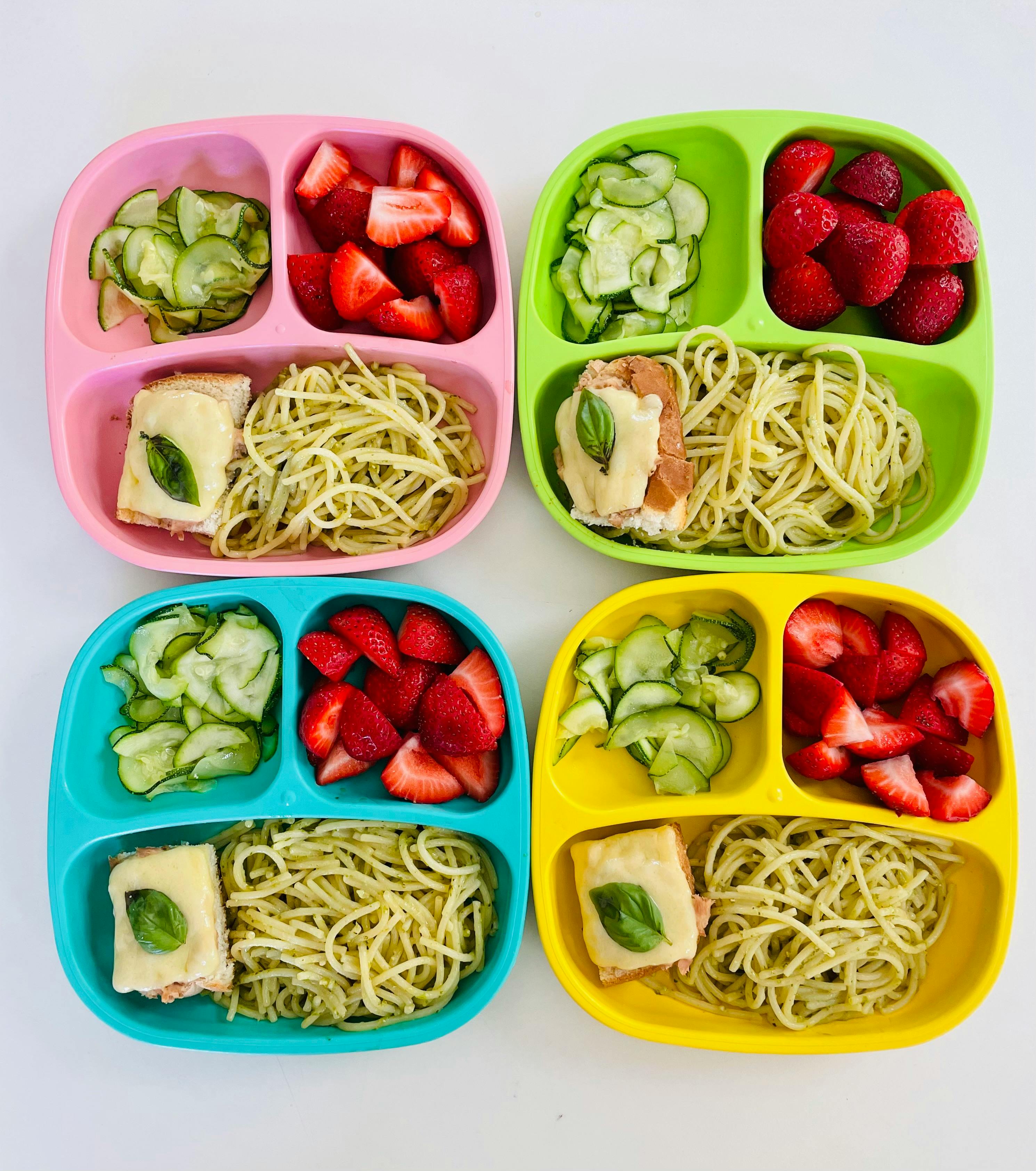 Four divided plates with pasta, strawberries, cucumbers, and a sandwich