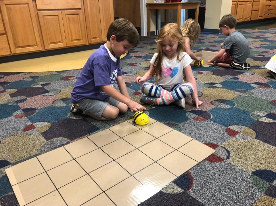 Two children playing with a bee-shaped robot on a grid
