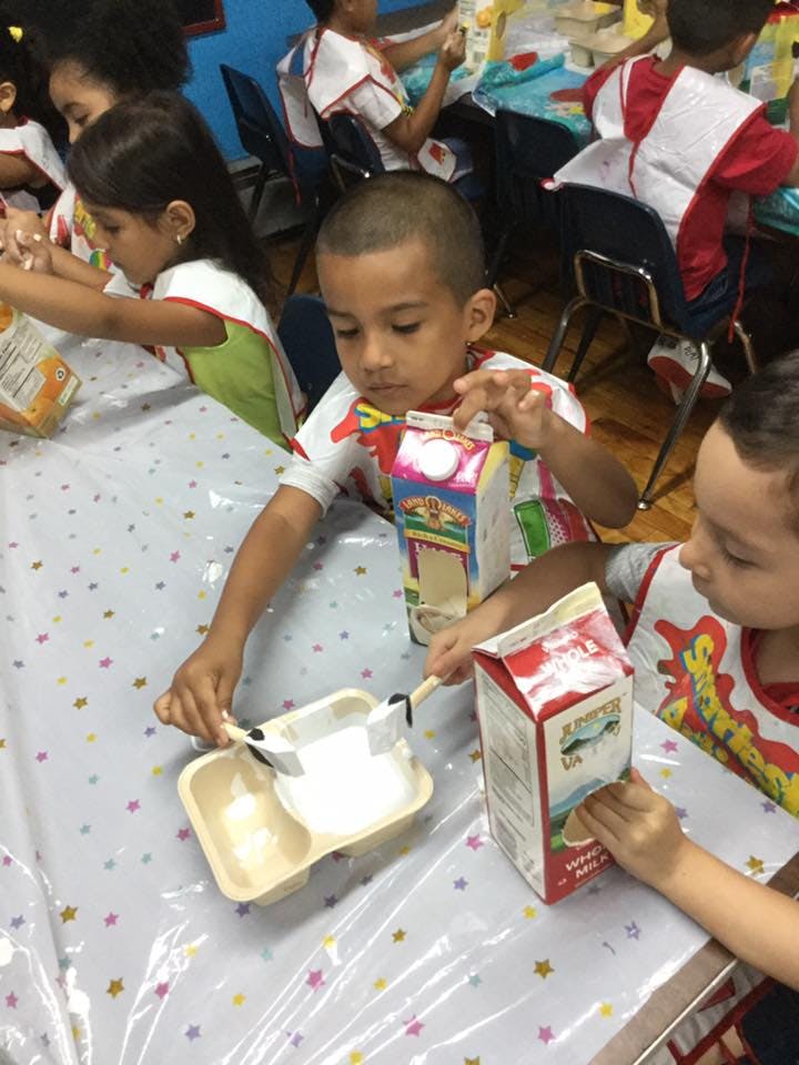 Child holding a milk carton and stirring a white substance in a tray
