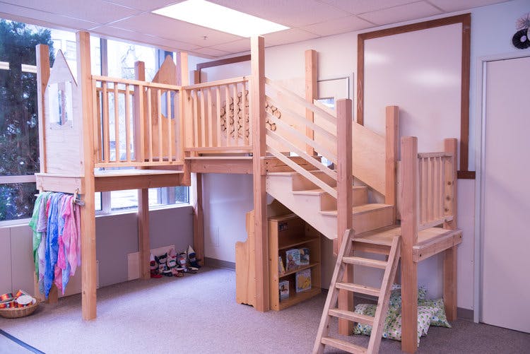 Indoor wooden play structure with stairs, ladder, and elevated platforms