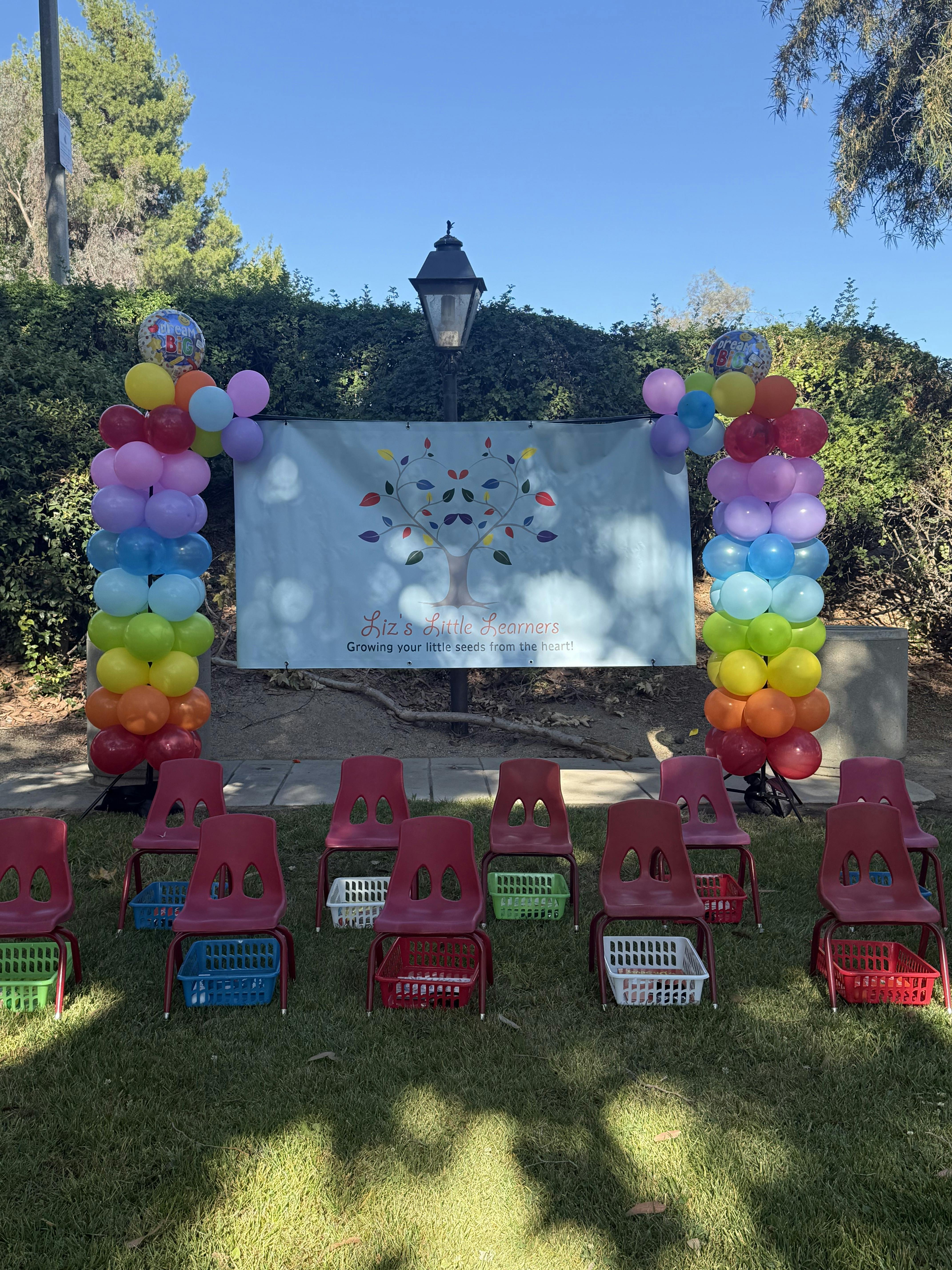 Banner for Liz's Little Learners surrounded by balloon columns and empty chairs