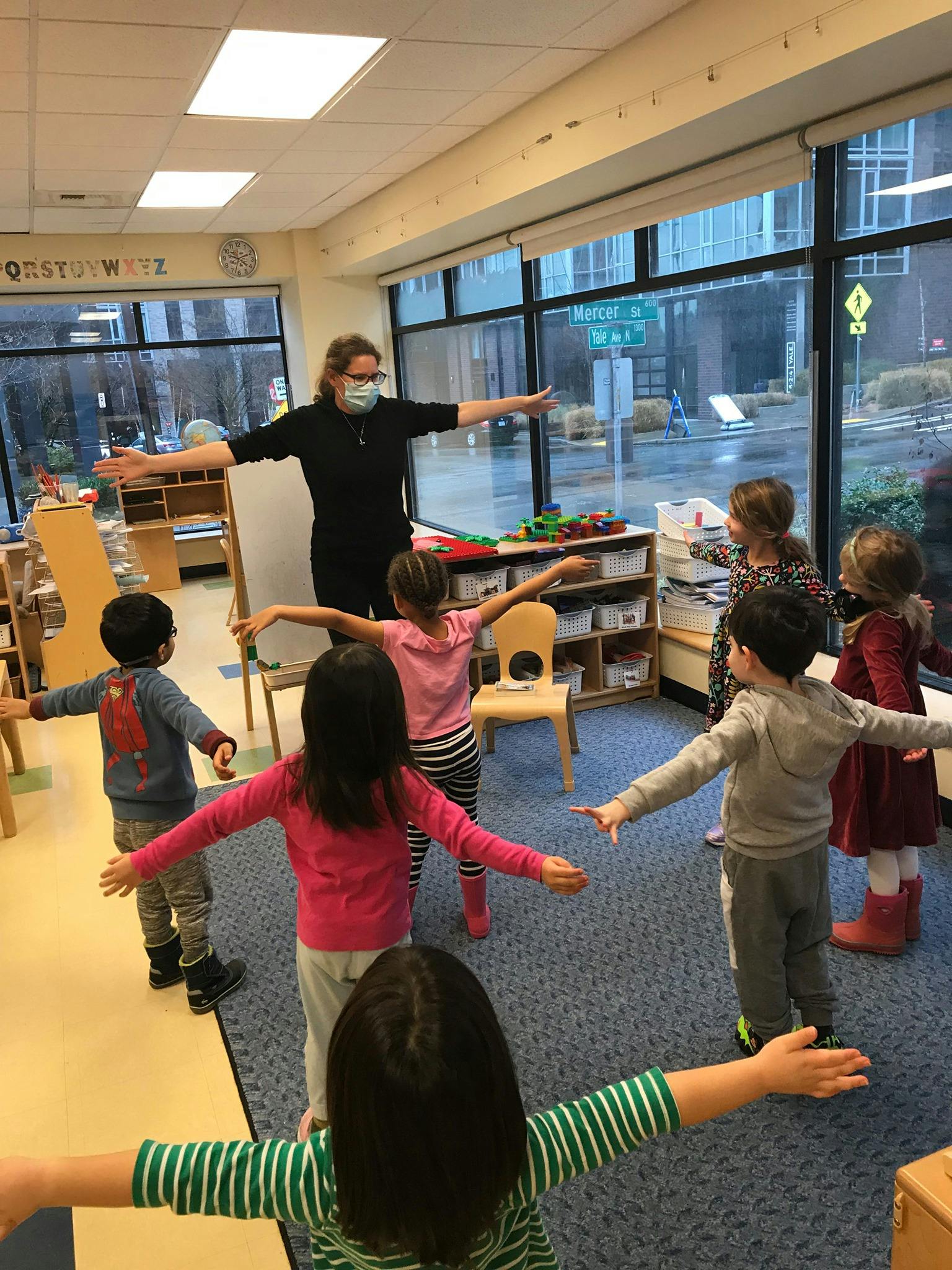 Adult and children standing in a classroom with arms outstretched