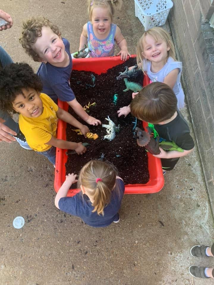 Children playing with toy animals in a red bin filled with dirt