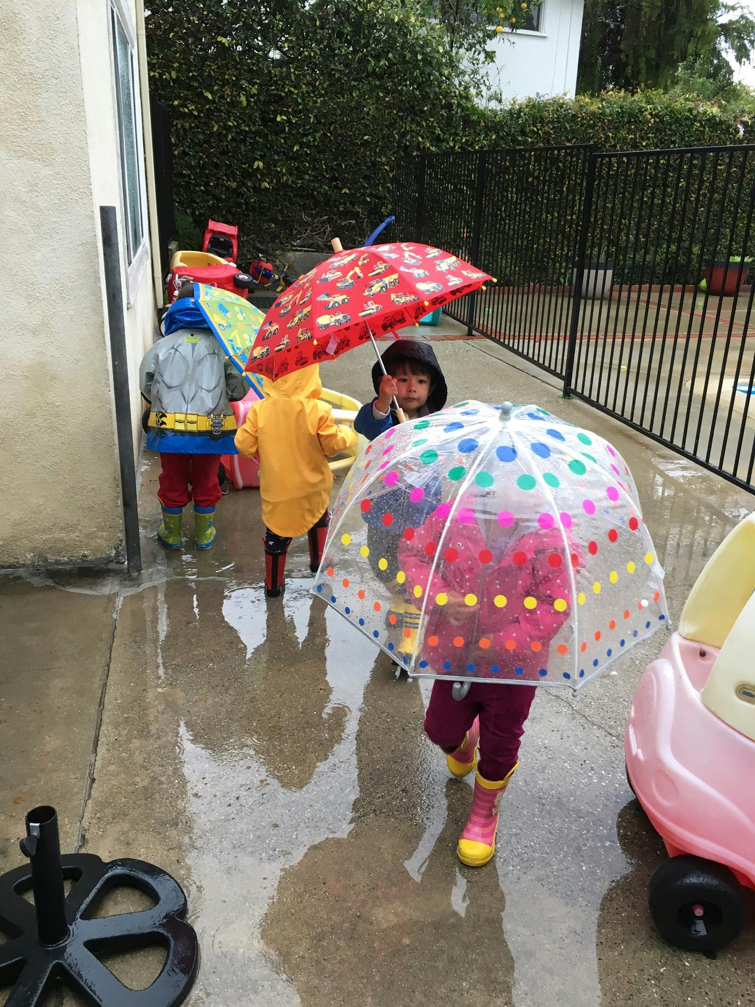 Children in rain gear holding umbrellas on a wet surface