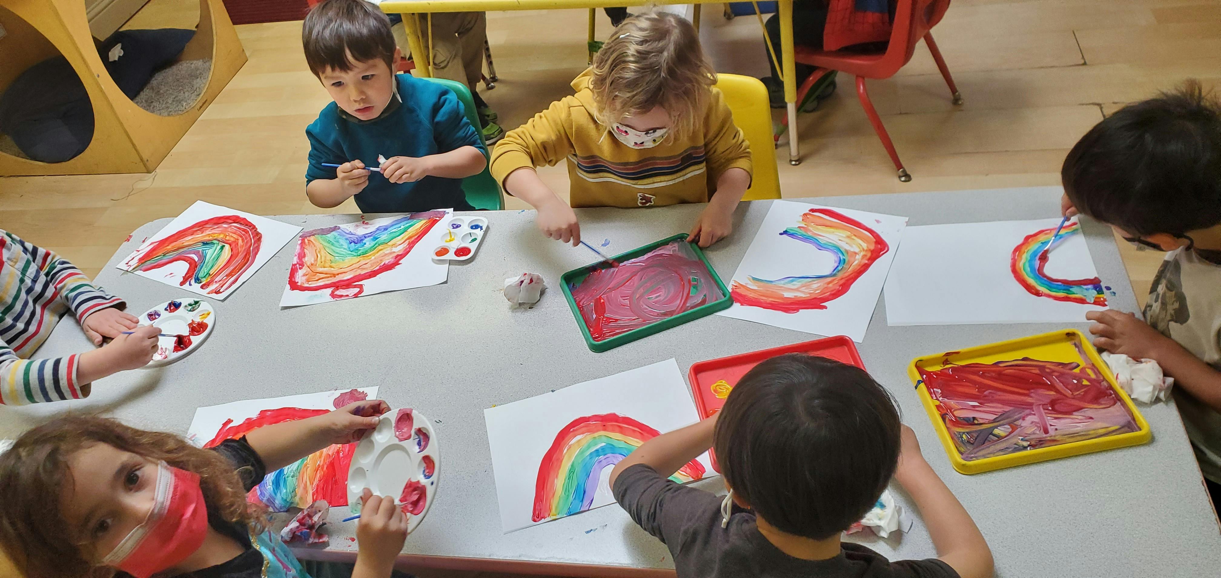 Children painting rainbows at a table
