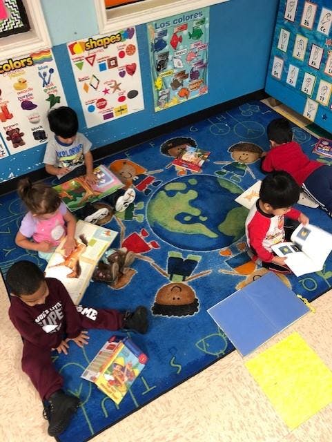 Children sitting on a rug and looking at books in a classroom