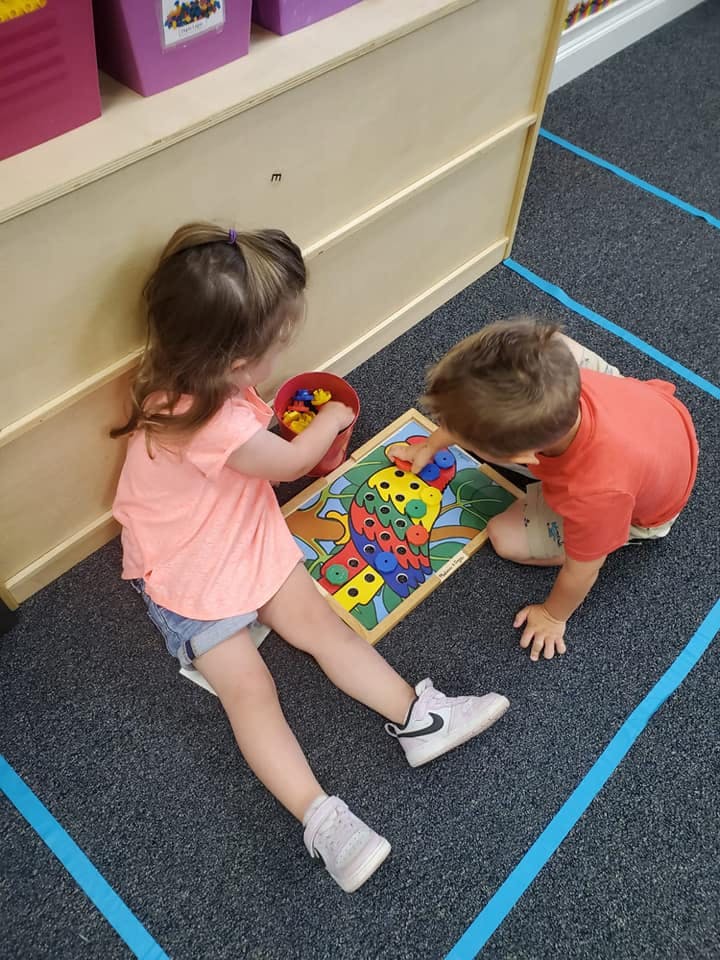 Two children playing with a colorful peg puzzle on the floor