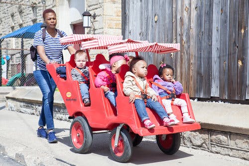 Person pushing a red multi-child stroller with four children
