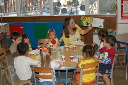 Adult reading a book to a group of children seated around a table