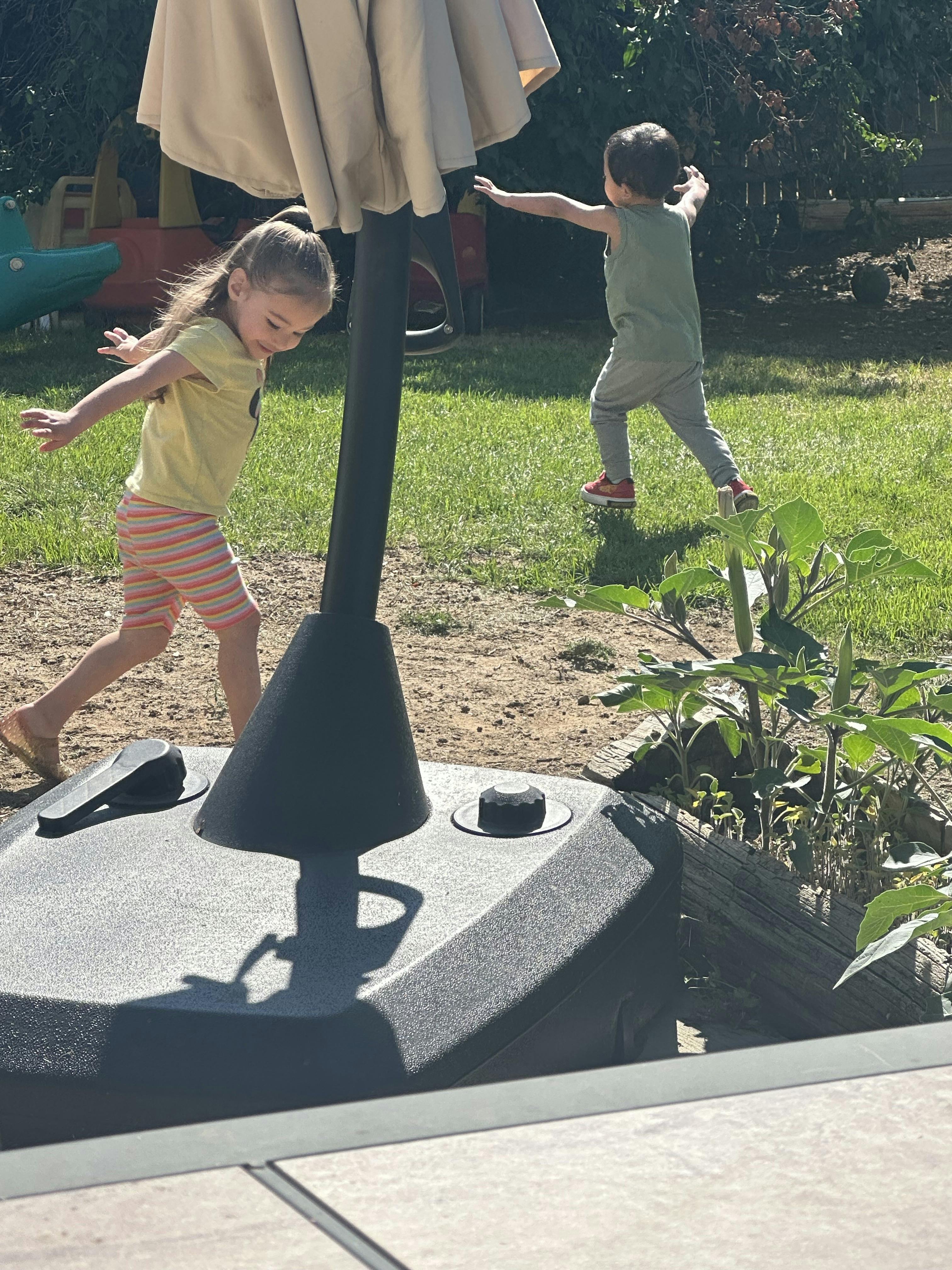 A child in striped shorts and a child in gray pants playing in a yard