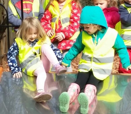 Two children in safety vests sitting on a slide