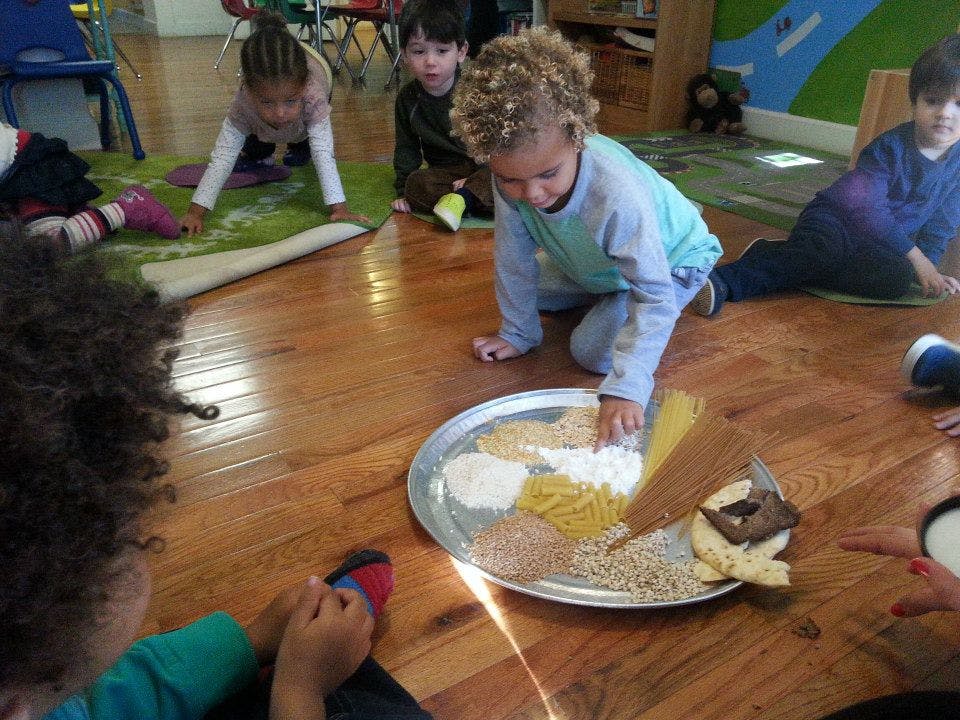 Child kneeling on floor touching items on a tray with other children nearby