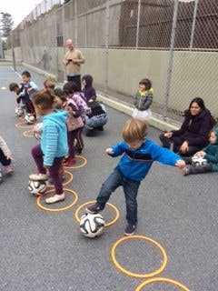 Children playing soccer with a coach on an outdoor court