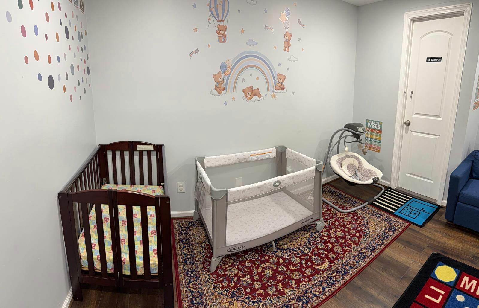 A nursery room with a crib, playpen, baby swing, and cartoon wall decals