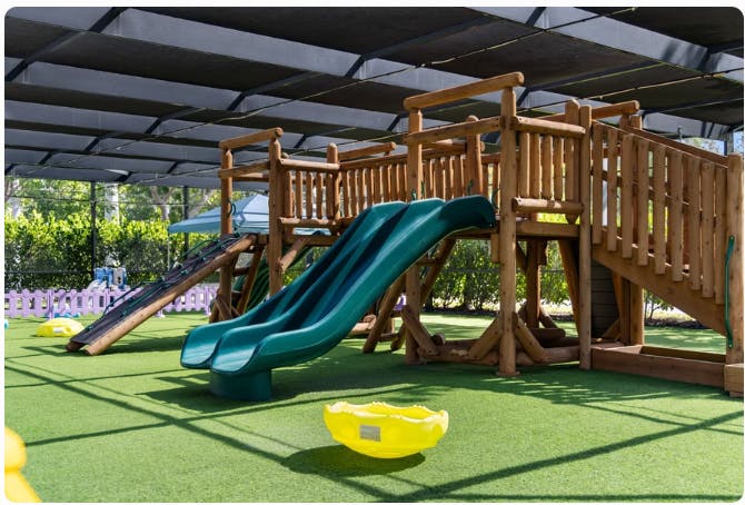 Children's playground with wooden structure, two green slides, and artificial turf