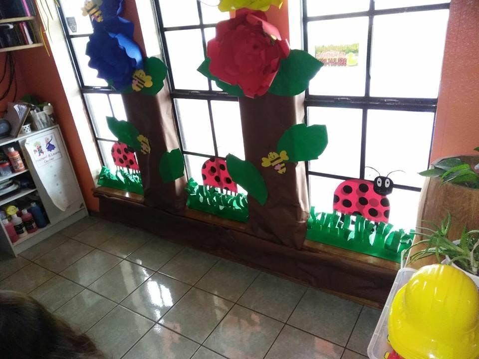 Window decorated with paper ladybugs, grass, and flowers