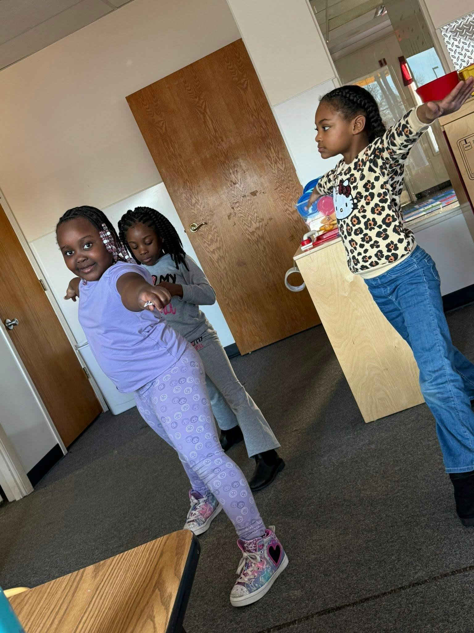Three children standing in a room, two with arms out like dancing