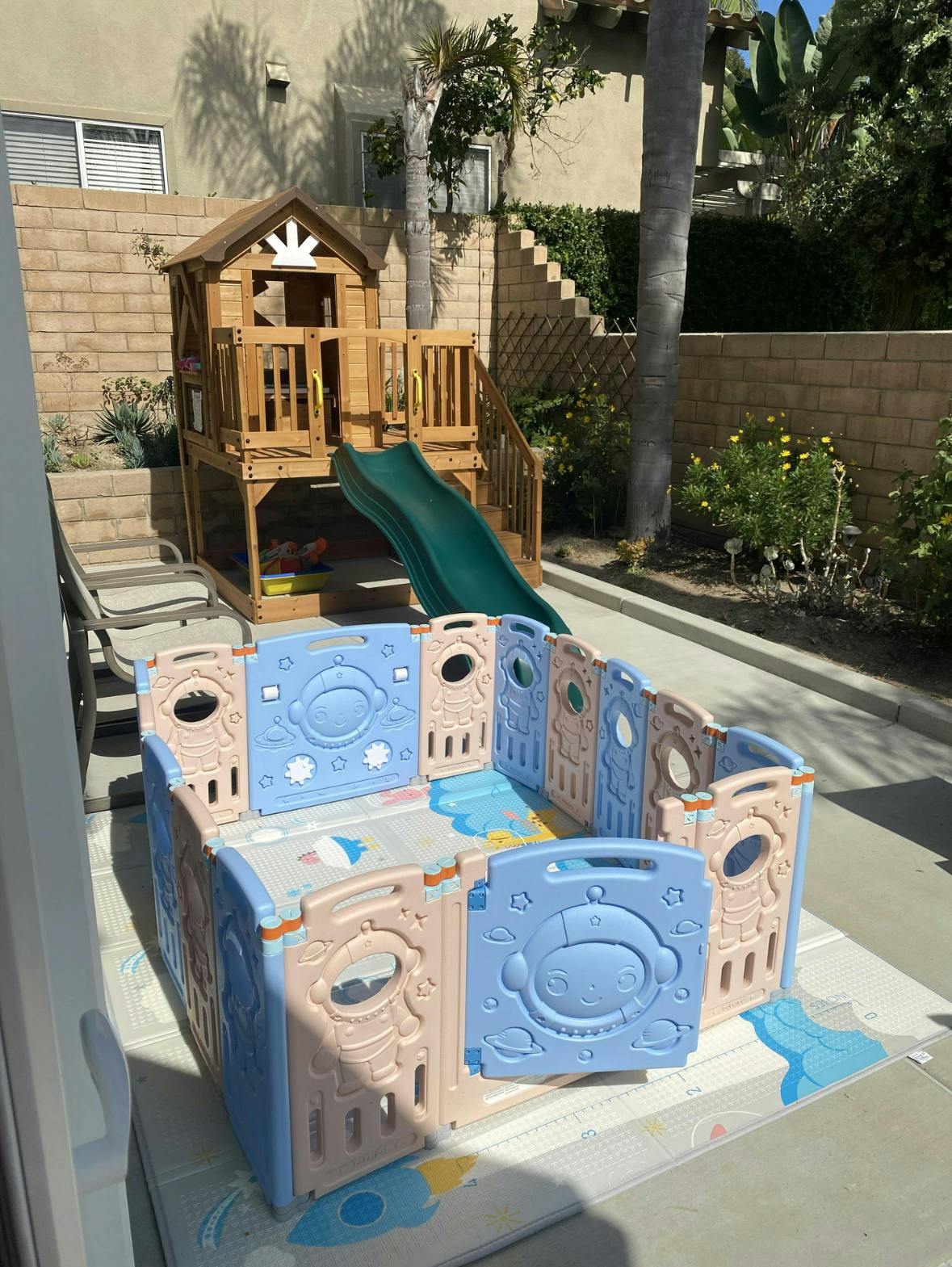 Wooden playhouse with slide next to a plastic playpen