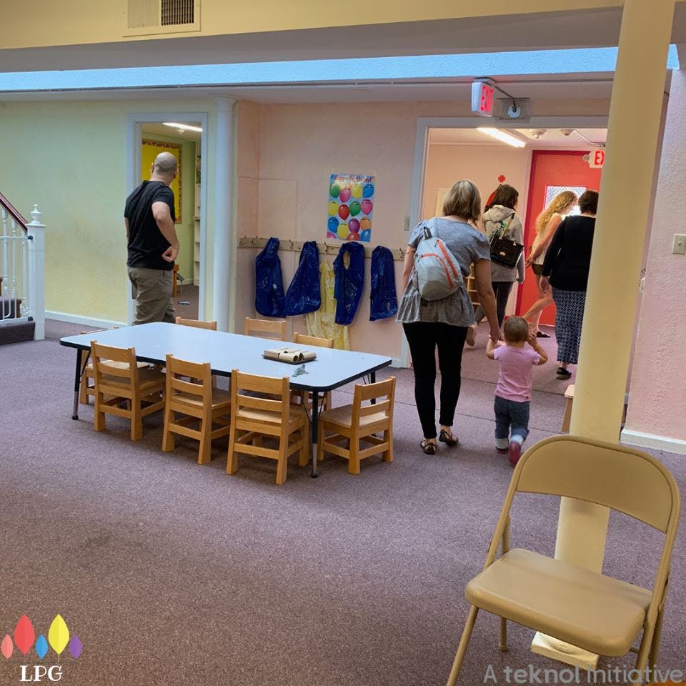 People and a child walking in a hallway past a table with small chairs