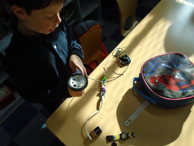 Child holding a small flashlight over a table with various objects