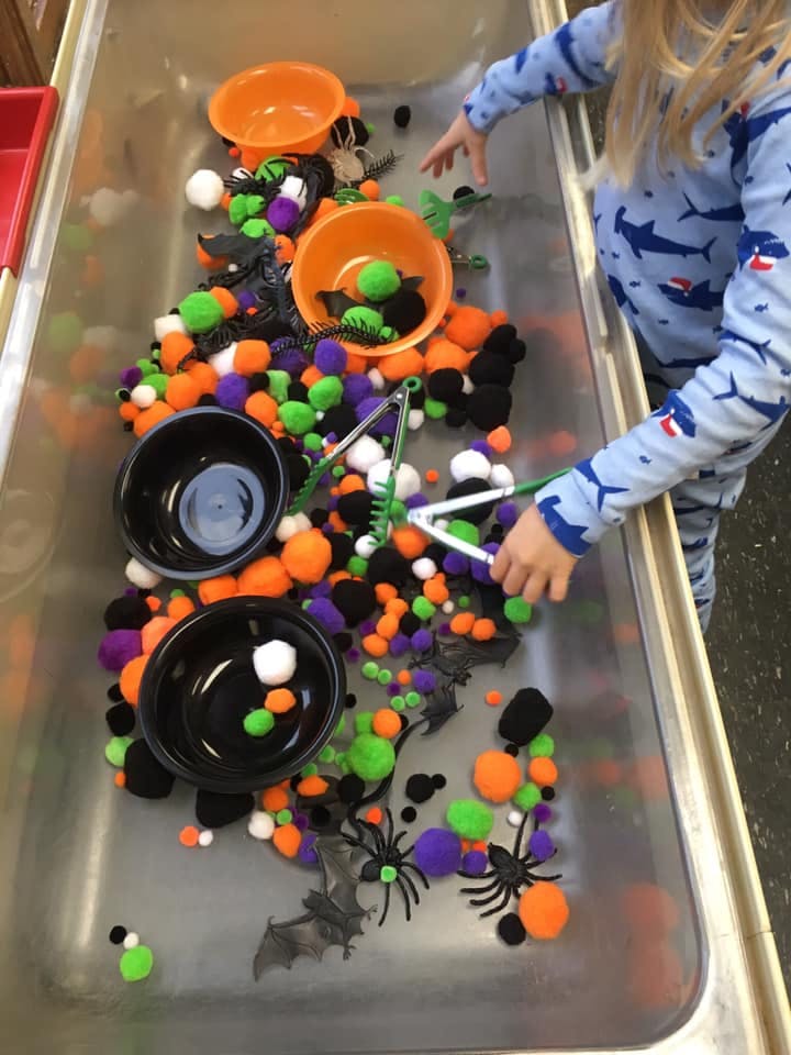 Child playing with pom-poms, plastic spiders, and bats in a sensory bin