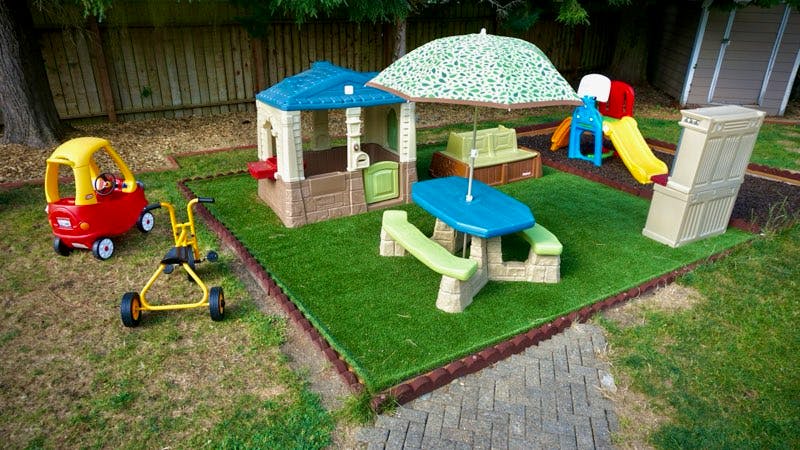 Children's play area with playhouse, picnic table, umbrella, and toy car