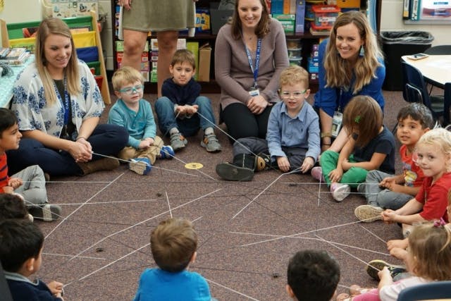 Adults and children sitting on the floor with string and small objects