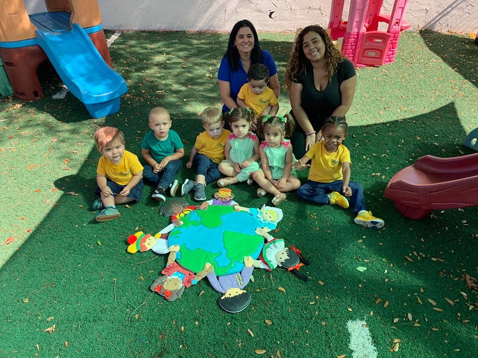 Two people and several children sitting on grass with a large earth cutout
