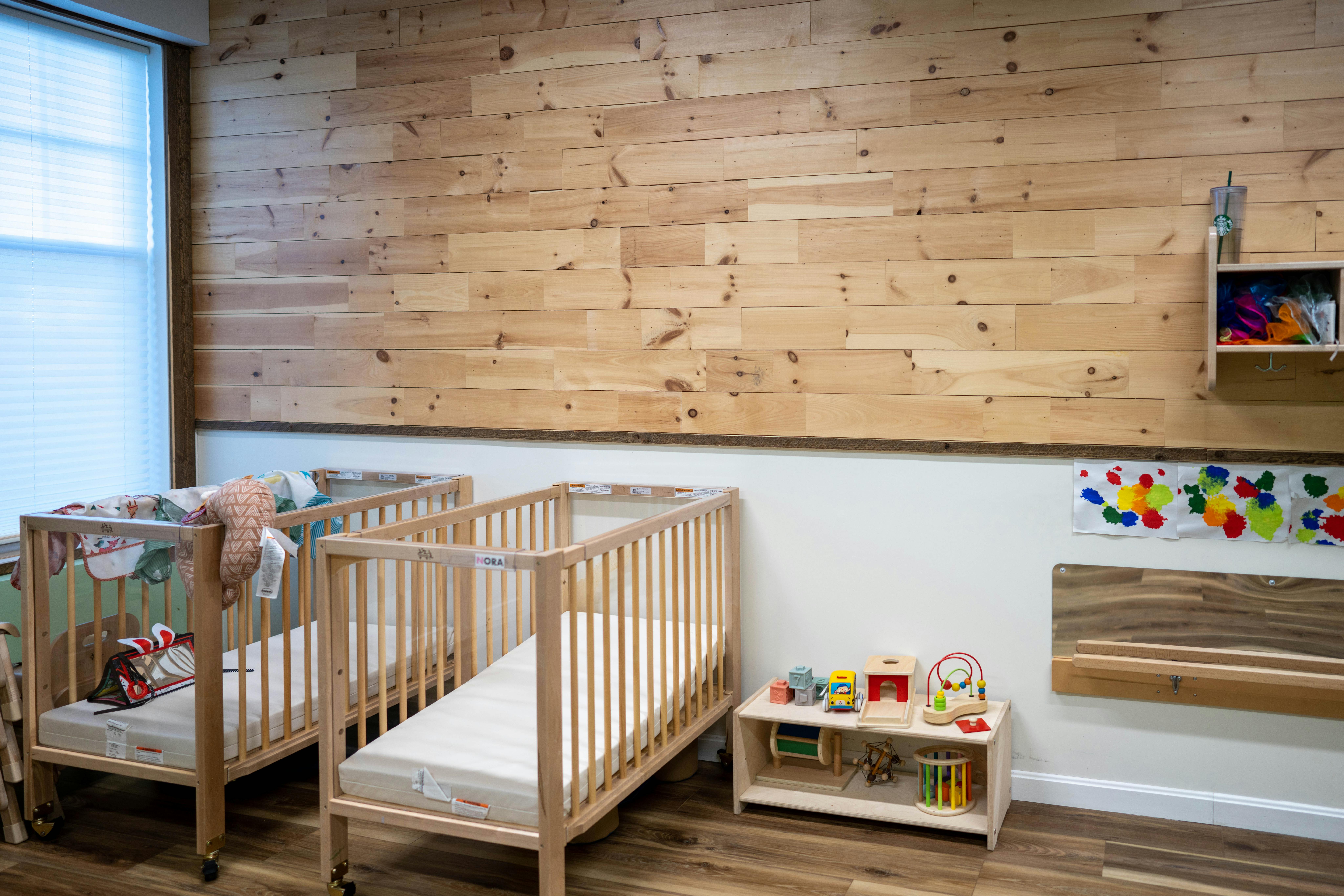 Two empty cribs in a room with a wooden accent wall