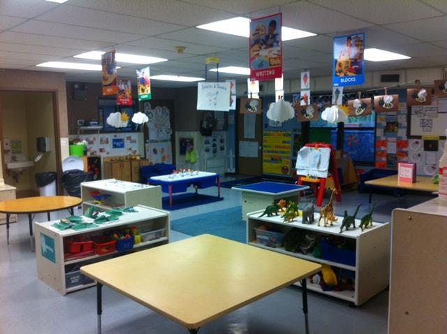 Empty classroom with small tables, shelves, and learning banners hanging from ceiling