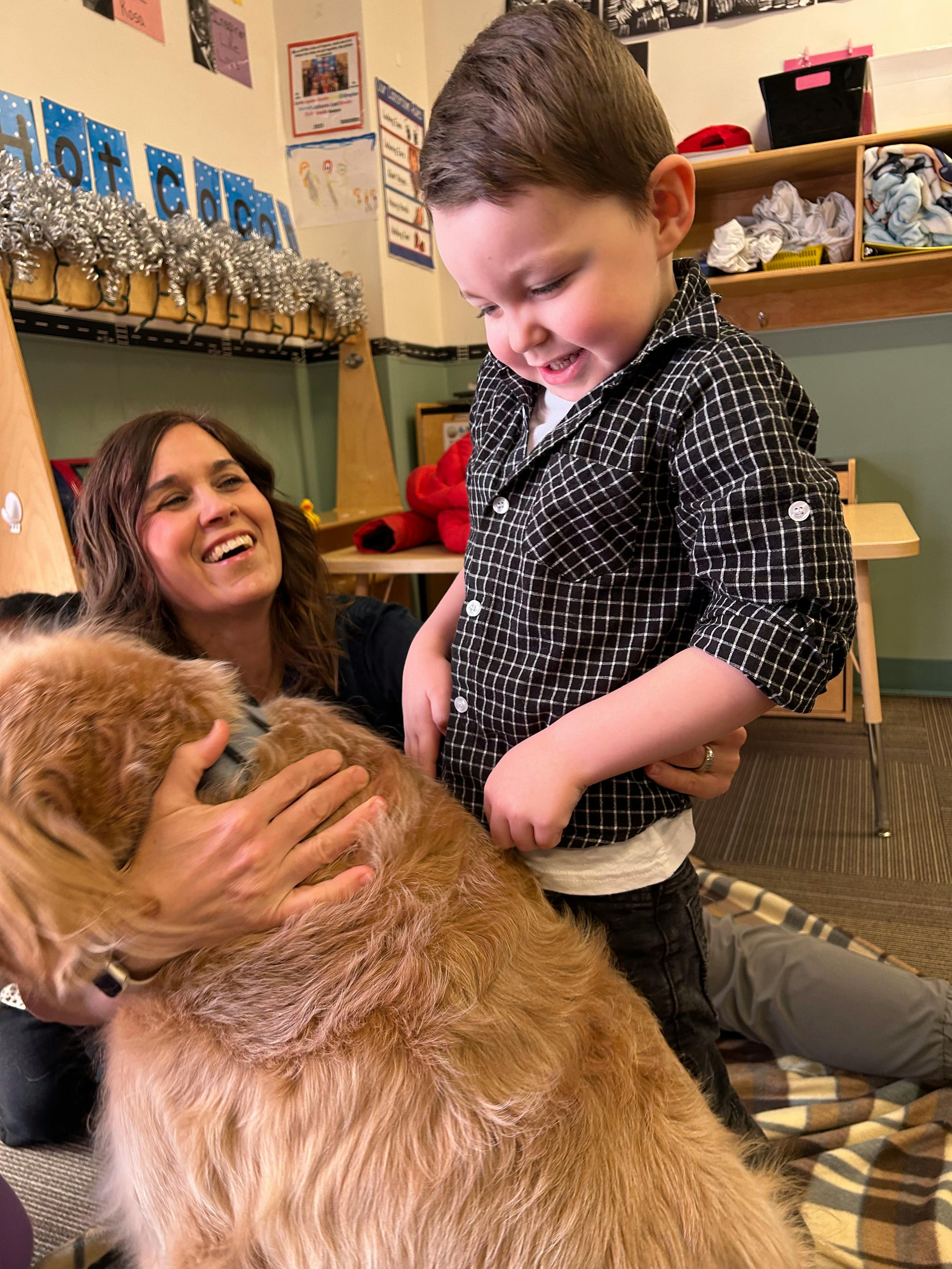 Child petting a golden retriever while a woman smiles in the background