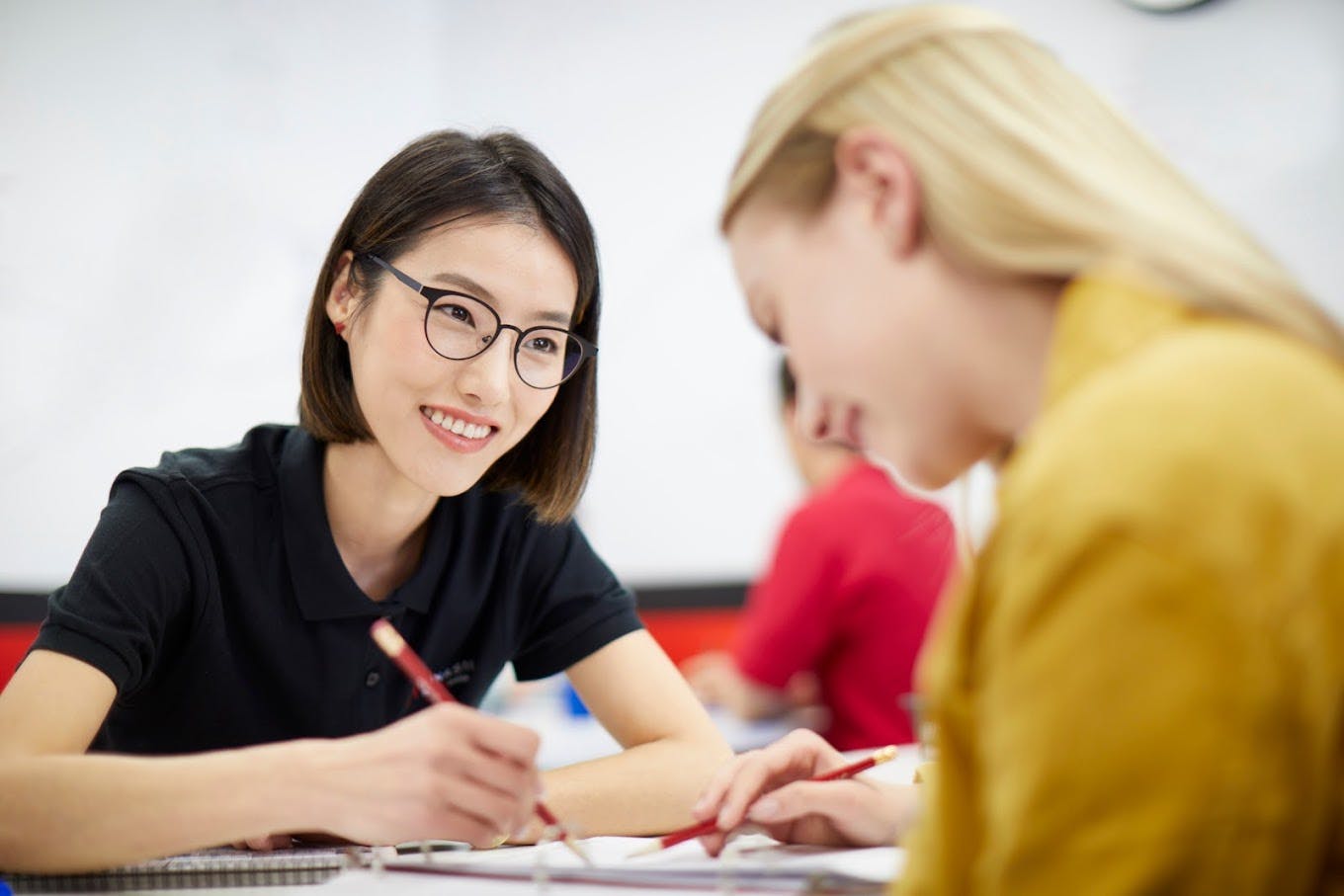 Two people writing and looking at papers in a classroom