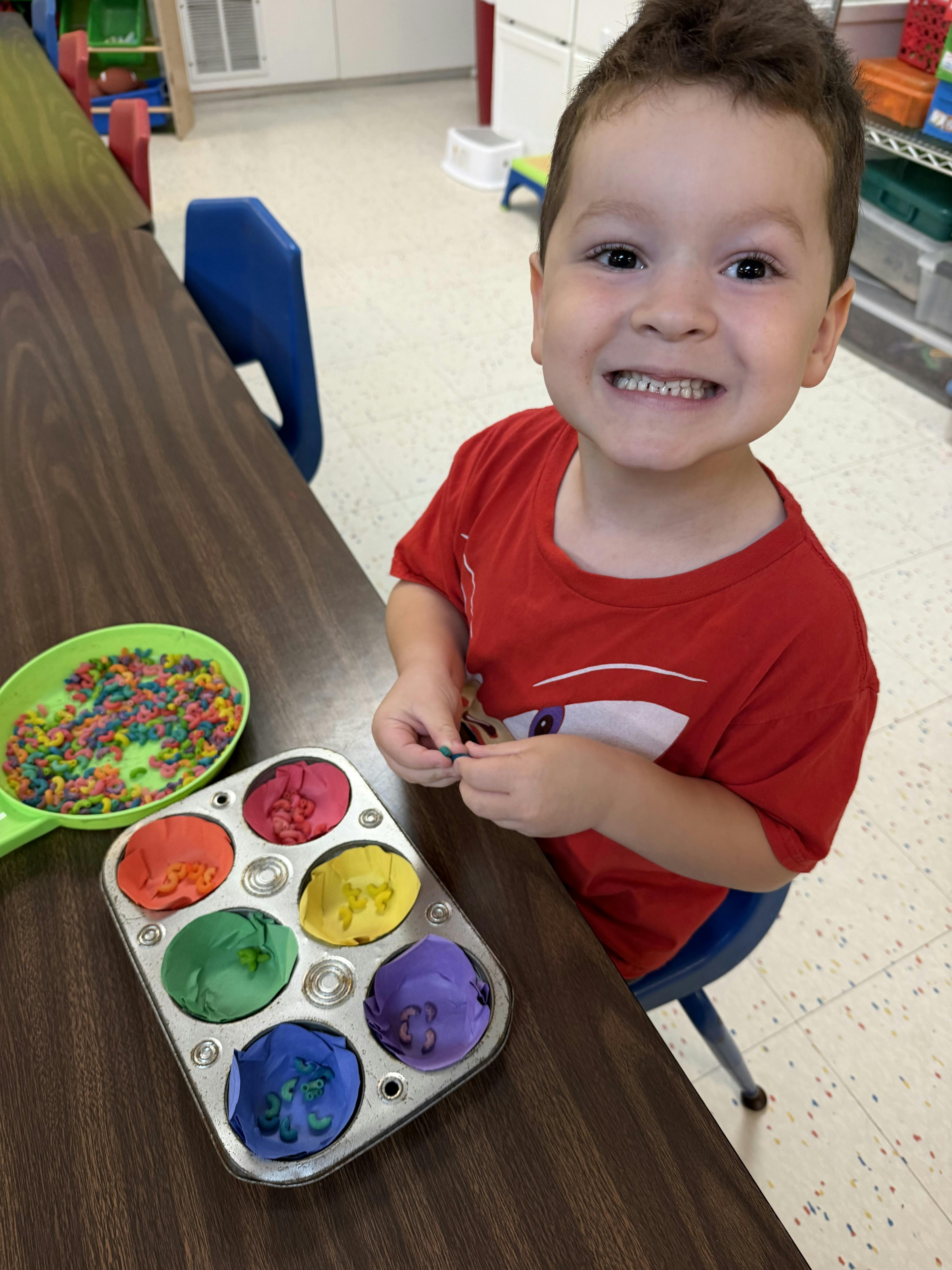 Child sorting colorful pasta into a muffin tin in a classroom