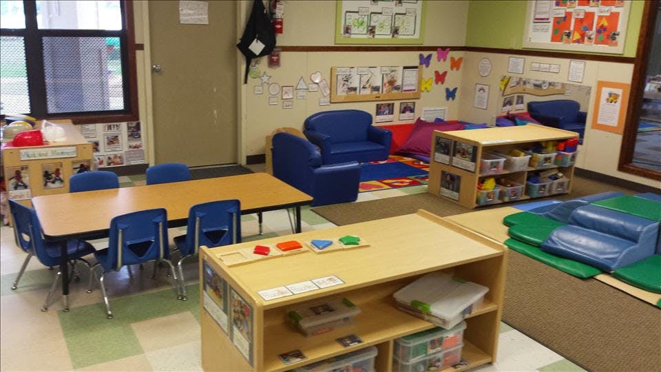 An empty early childhood classroom with small tables, chairs, and play areas