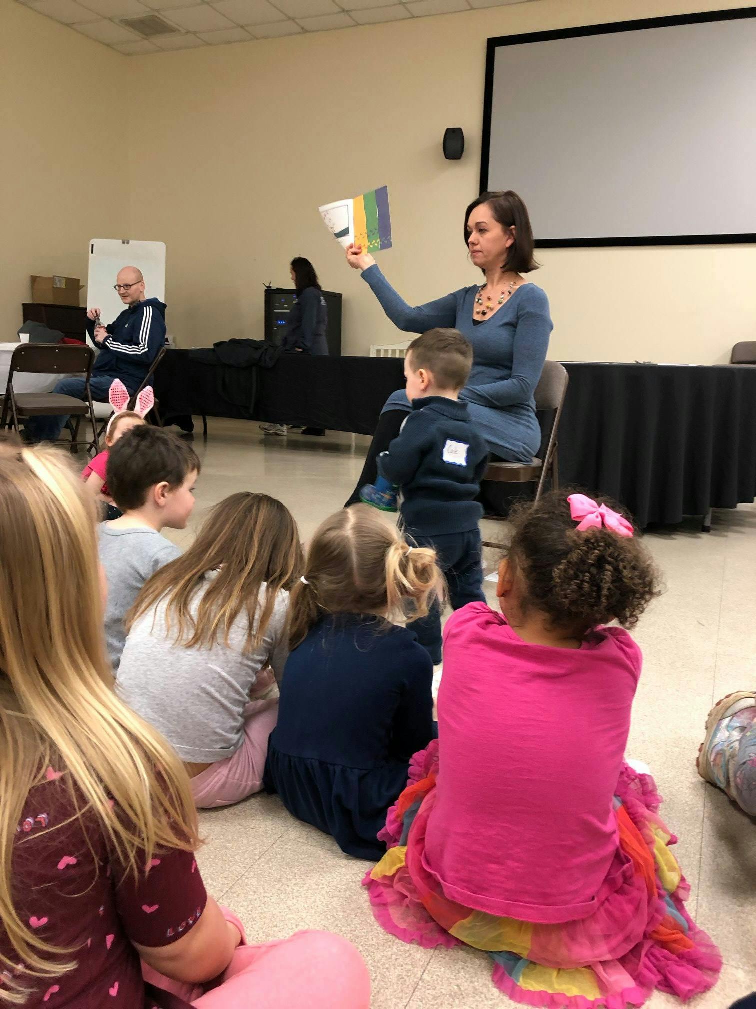 Adult reading a book to a group of children sitting on the floor