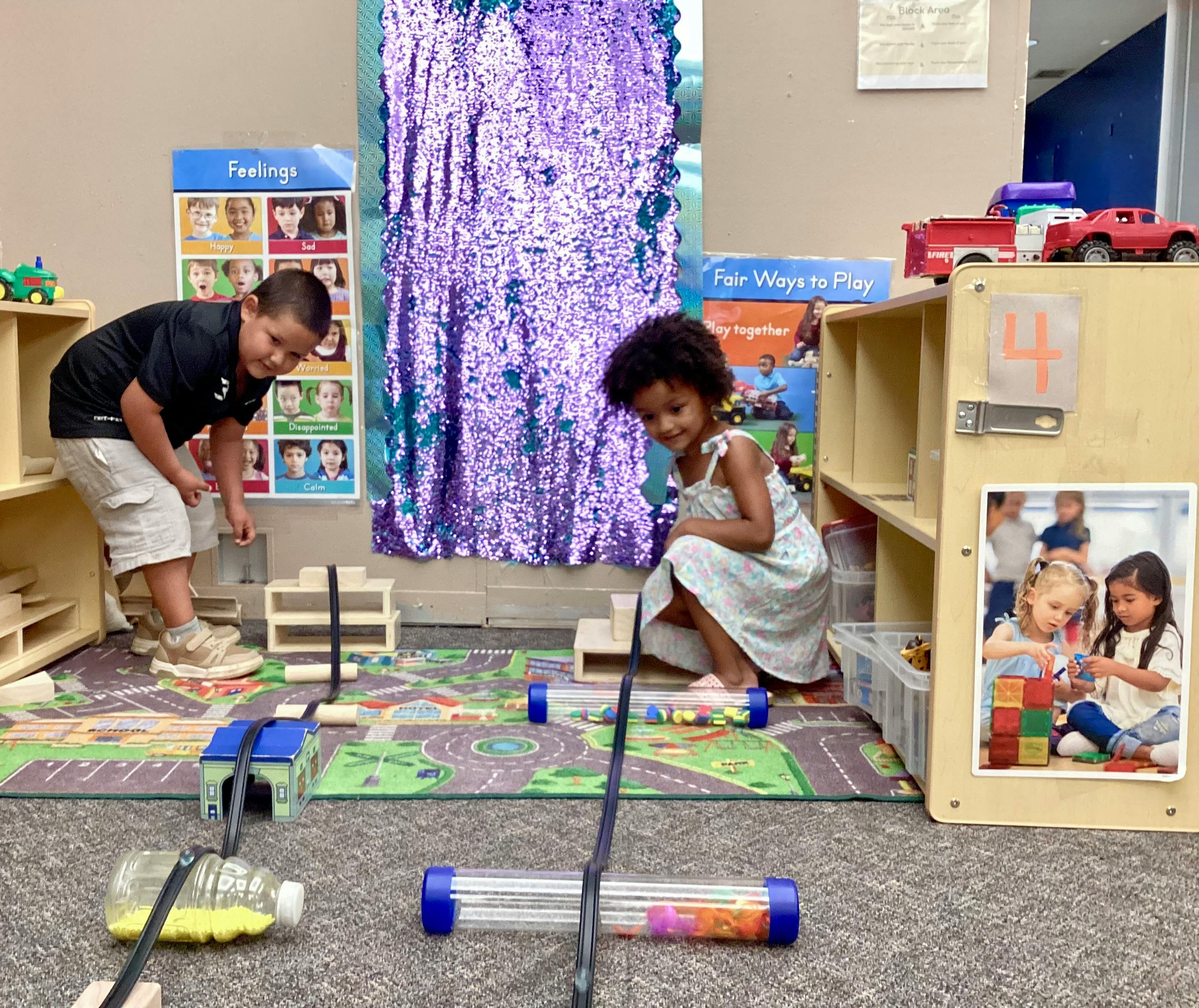 Two children playing with tracks and containers on a mat in a classroom