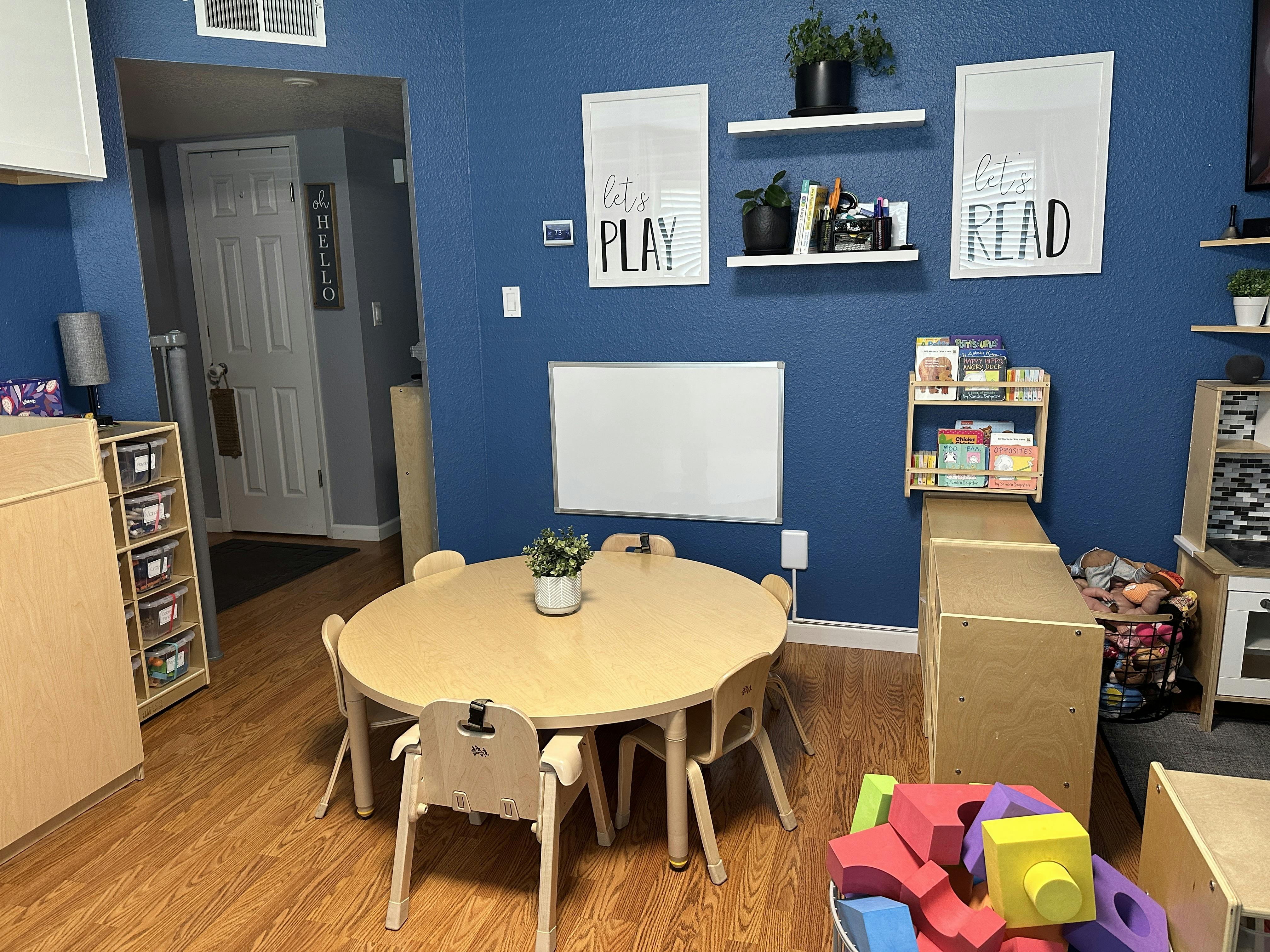 Children's classroom with a round table and chairs, shelves, and a whiteboard