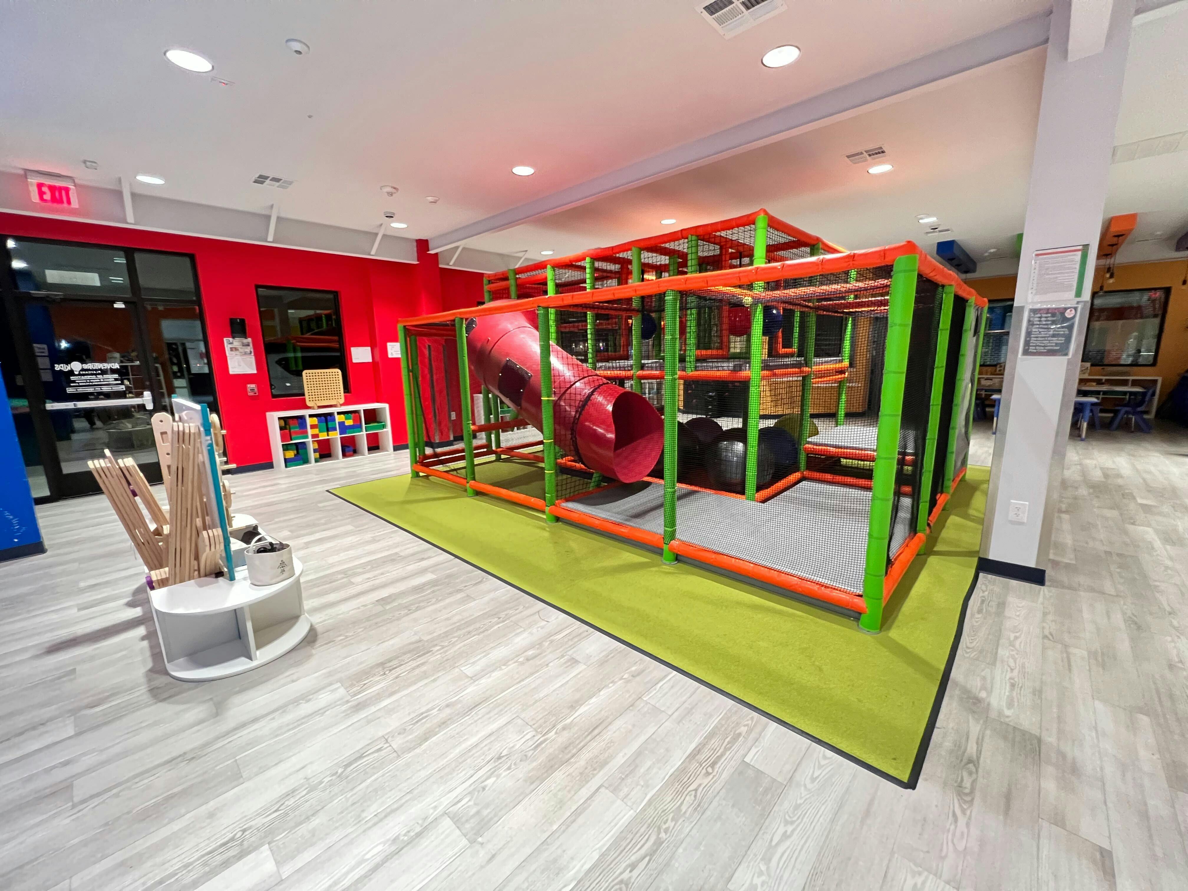 Indoor playground with red slide and green and orange climbing structure