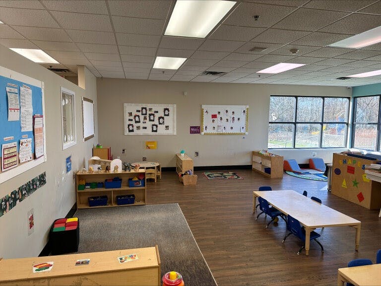 Empty classroom with small tables and chairs, shelves, and large windows