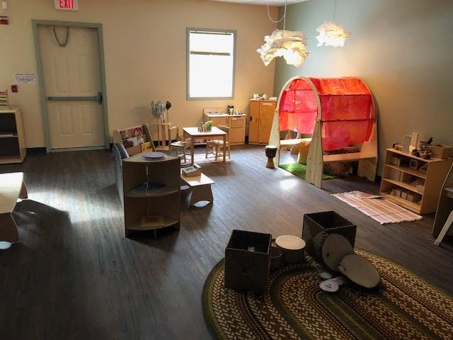 Classroom with small tables, chairs, and a red play tunnel