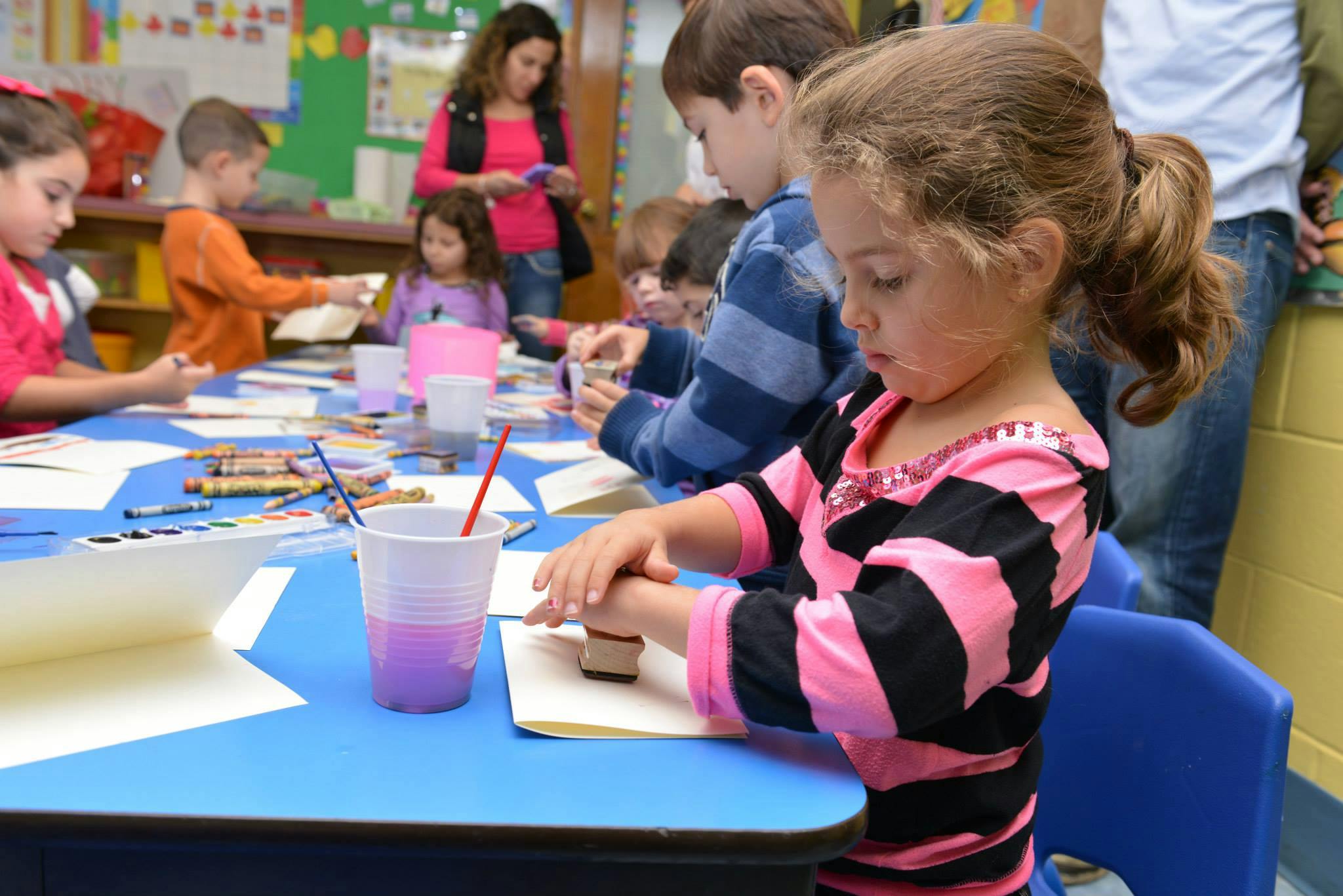Child at a table with other children and adults in a classroom