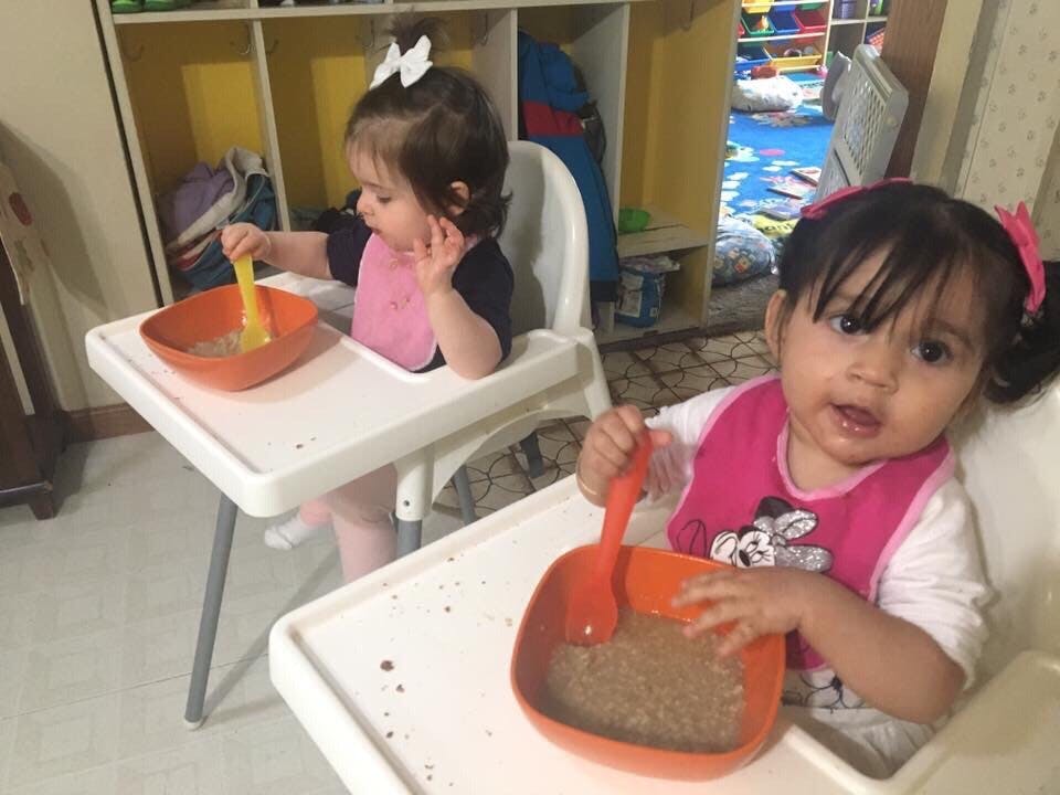 Two children in high chairs eating from bowls with spoons