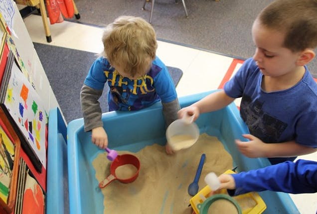 Two children playing with sand in a blue bin
