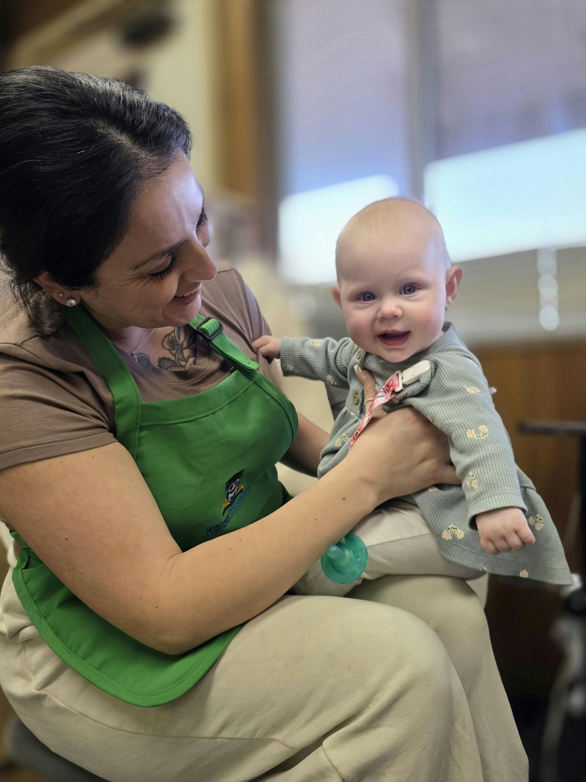 Person in green apron holding a child with a pacifier