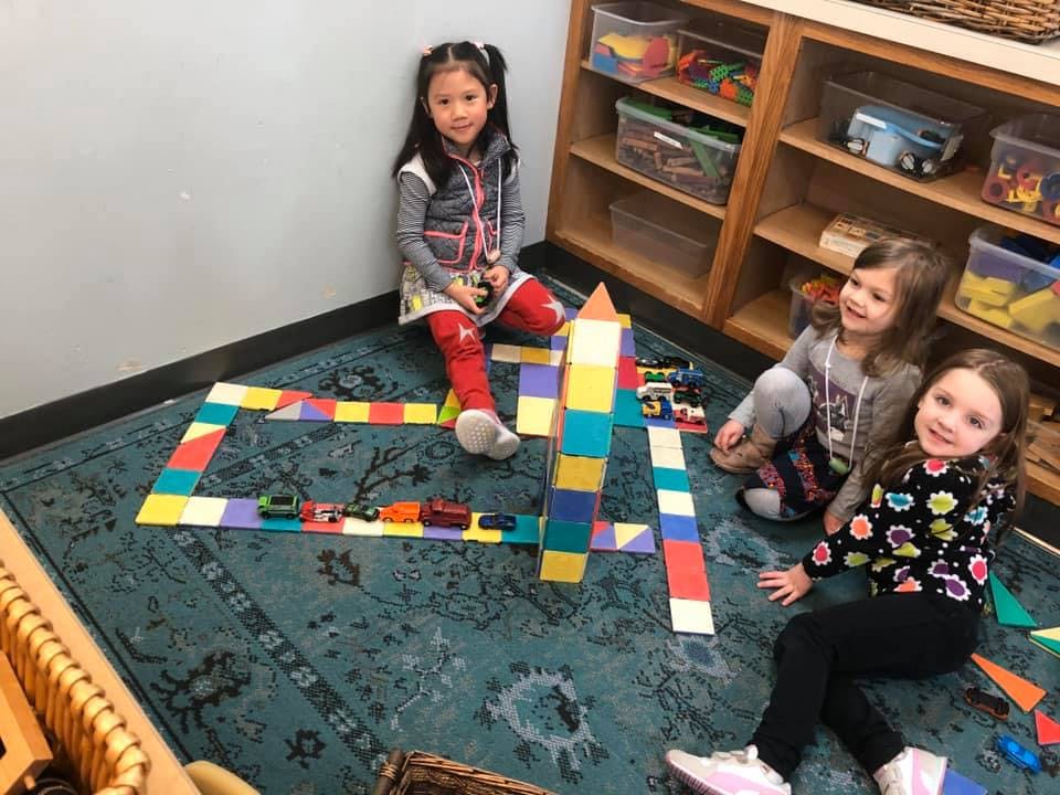 Three children playing with blocks and toy cars on a rug