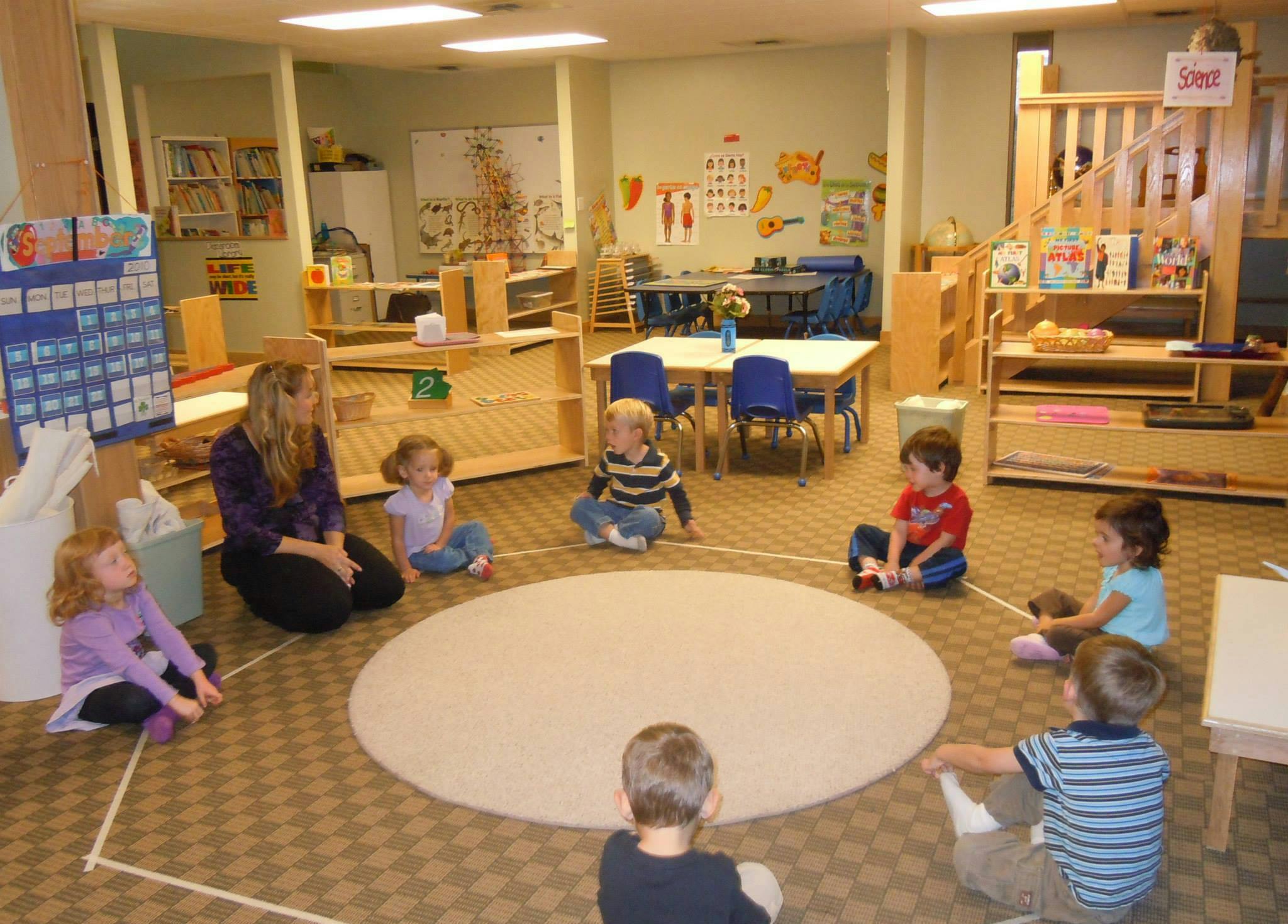 Adult and children sitting in a circle on a rug in a classroom