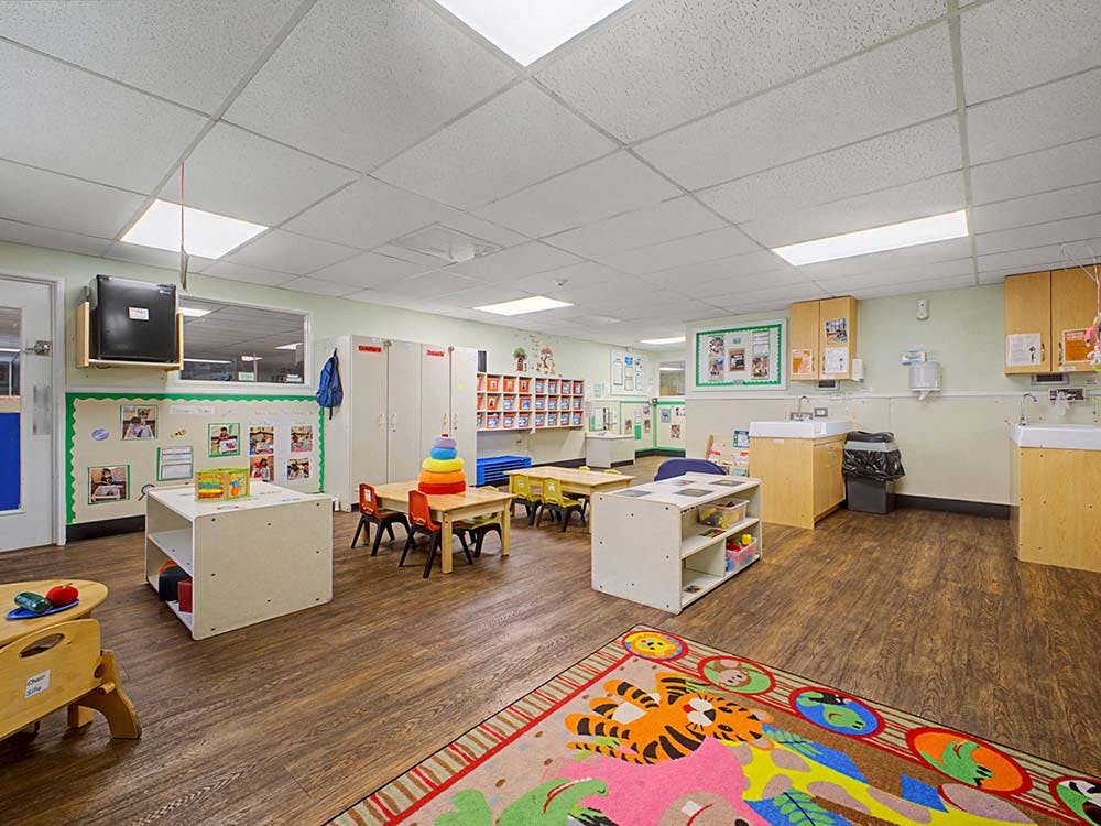 Empty classroom with small tables and chairs, shelves, and a colorful rug